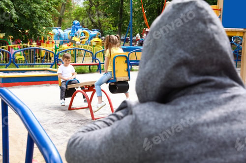 Preview: Suspicious adult man spying on kids at playground, space for text. Child in danger