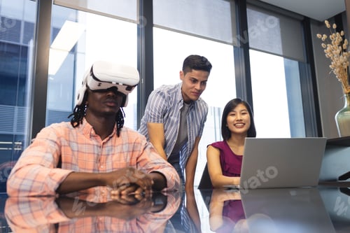 Preview: Diverse group of colleagues exploring virtual reality and using laptop in a modern business office