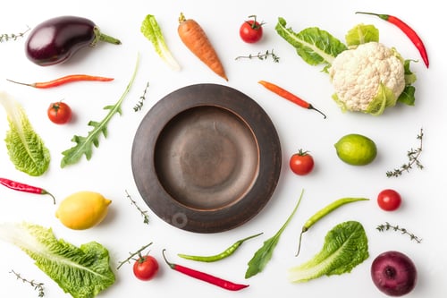 Preview: Top view of plate among uncooked vegetables isolated on white