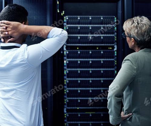 Preview: Rearview shot of two technicians looking stressed while working in a data centre