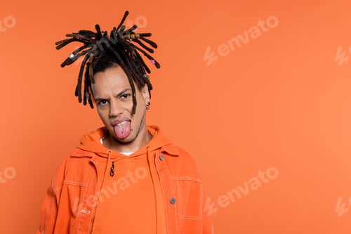 Preview: pierced and multiracial man with dreadlocks looking at camera while sticking out tongue isolated on
