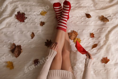Preview: Woman in warm socks with dry leaves on knitted blanket, top view