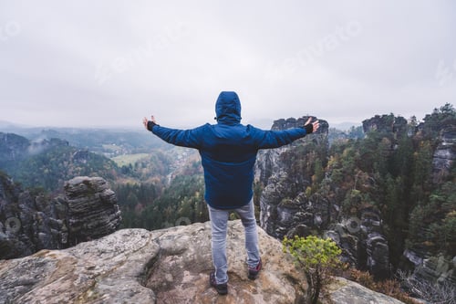Preview: Hiker in outdoor clothing raised hands on the top of a mountain and enjoying view of cliffs ridge