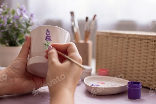 Preview: Girl's hands draw a lavender flower on a white ceramic pot