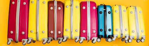 Preview: colorful travel bags in stack isolated on yellow, panoramic shot