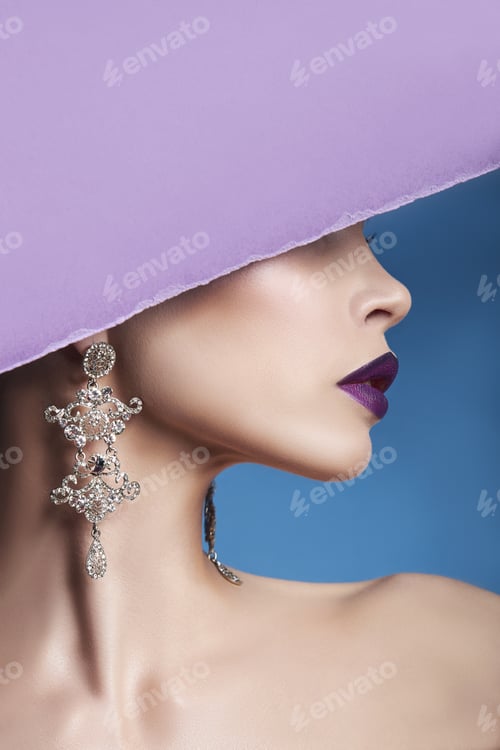 Preview: Earrings and jewelry in ear of a sexy woman pressed against the paper purple. Perfect brunette girl