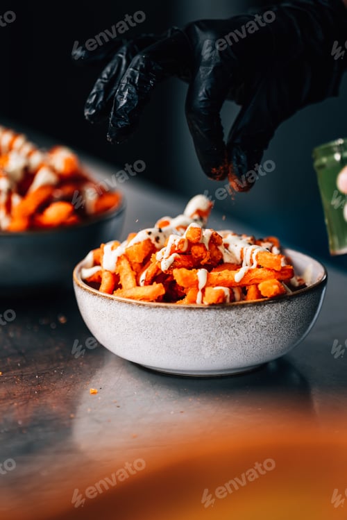 Preview: Vertical shot of a cook sprinkling pepper on fried food on the table