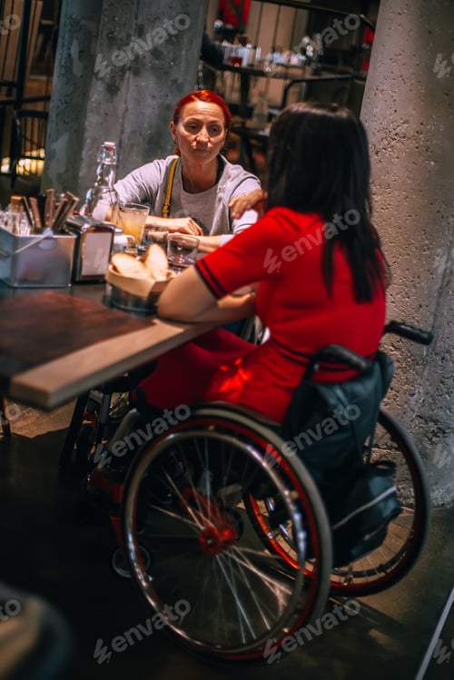 Preview: Two girls in wheelchairs in cozy cafe waiting for order.