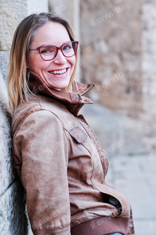 Preview: Woman with eyeglasses smiling while posing outdoors.
