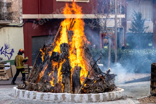 Preview: Fire in a bonfire with firewood burning and firefighters in the background.