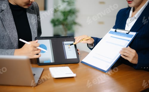 Preview: Two professional women in suits reviewing financial charts and analytics on paper and tablet