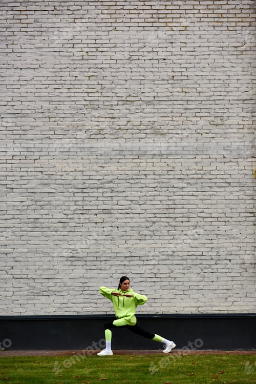 Preview: active sportswoman in lime color hoodie and leggings doing lunges while exercising outdoors