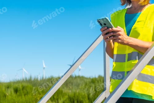 Preview: Woman worker in a wind farm, green energy, technical review, with the phone in her hand