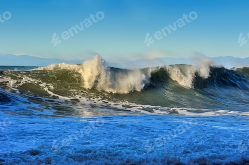 Preview: powerful great waves on the sea crests with foam, mountains in the distance on the horizon