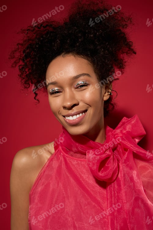 Preview: Vibrant young woman smiling brightly against a bold red background in a joyful moment