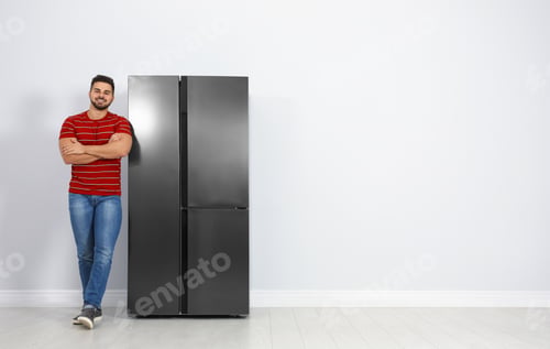 Preview: Happy young man near refrigerator indoors, space for text