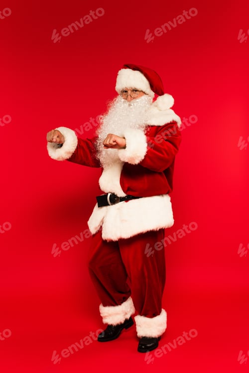 Preview: Bearded santa claus looking at camera while dancing on red background