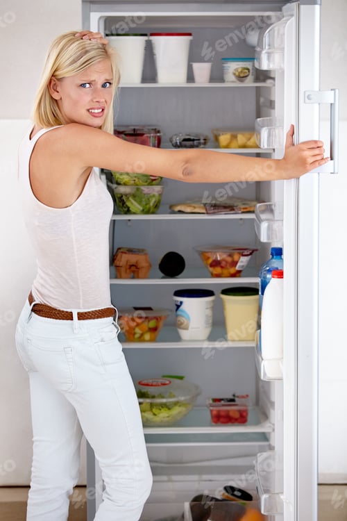 Preview: Tempted to cheat on her diet. Portrait of a worried young woman looking in her fridge.