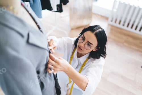 Preview: Focused woman with coat on dummy stand and stitching up in shop