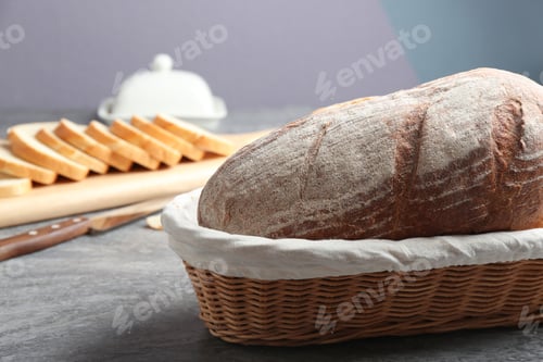 Preview: Loaf of tasty fresh bread in wicker basket on grey table, closeup