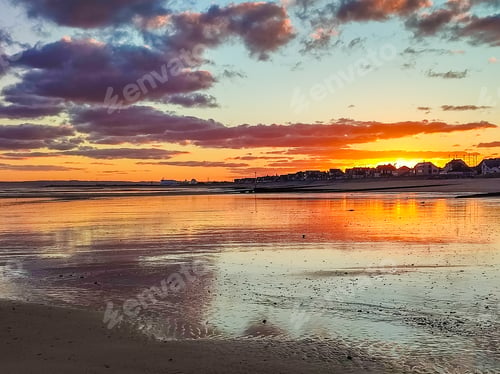 Preview: Sunset lights up the beach with rich colors, casting reflections on the still water as the day ends