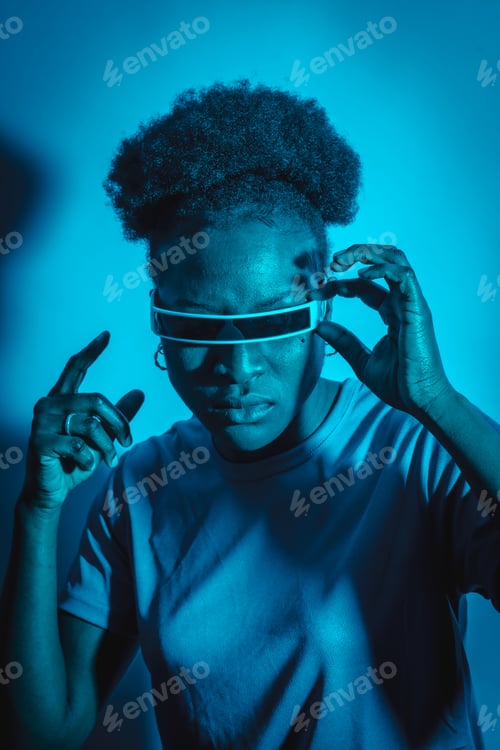 Preview: Young African American woman isolated on a blue background with futuristic glasses, studio shoot
