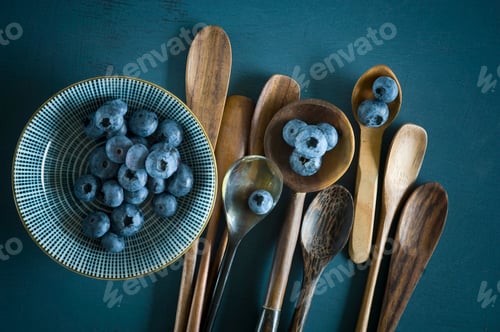 Preview: Bowl of blueberries and different spoons on blue ground