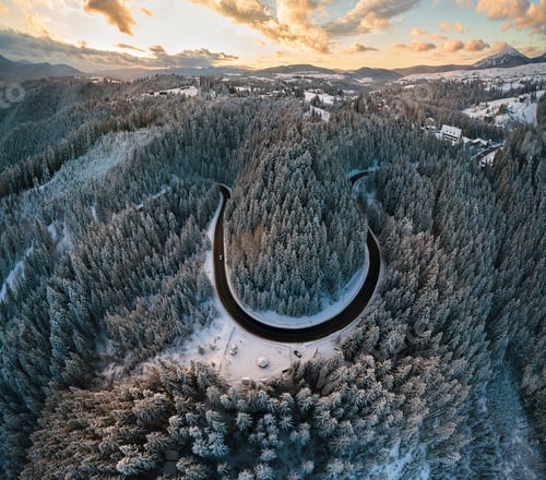Preview: Aerial view of winter landscape with snow covered mountain hills and winding forest road in morning.