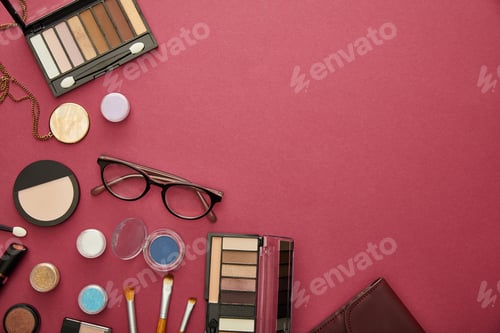 Preview: top view of decorative cosmetics near glasses and necklace on crimson