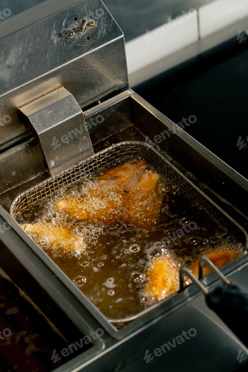 Preview: close-up in a professional kitchen frying chicken wings in oil in a deep fryer