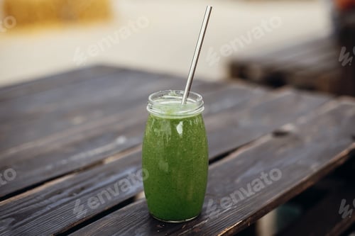 Preview: Healthy spinach smoothie in glass jar with metal reusable straw on wooden table