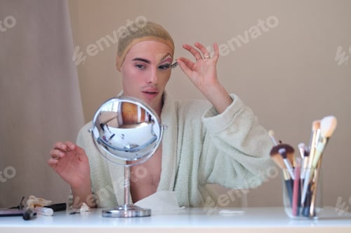 Preview: Drag queen person removing false eyelashes and wearing bathrobe.