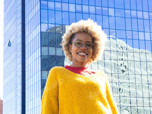 Preview: African American woman with headphones and with afro hair looking at camera in a city