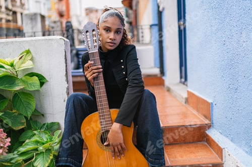 Preview: Young latin woman musician holding acoustic guitar on porch steps