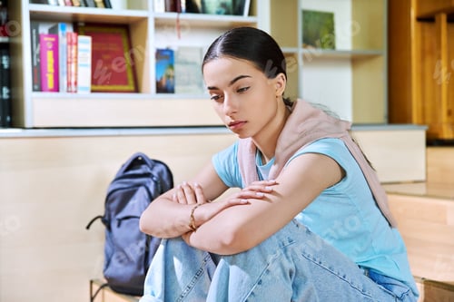 Preview: Upset sad teenage girl high school student sitting on floor in library classroom