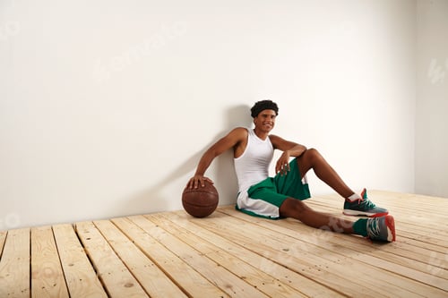 Preview: Handsome young black basketball player sitting on the wooden floor