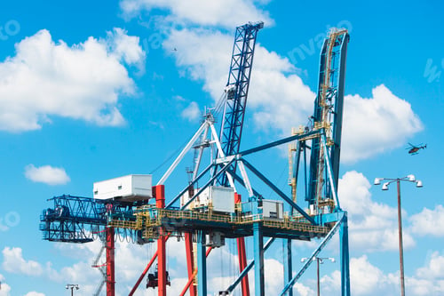 Preview: Cargo cranes at a shipping port under a blue sky.