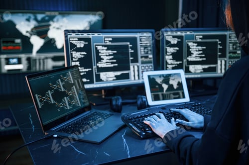 Preview: Young professional female hacker is indoors by computer with lot of information on displays