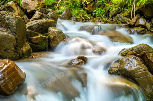 Preview: Mountain river with small waterfall with clear turquoise water falling down between wet boulders