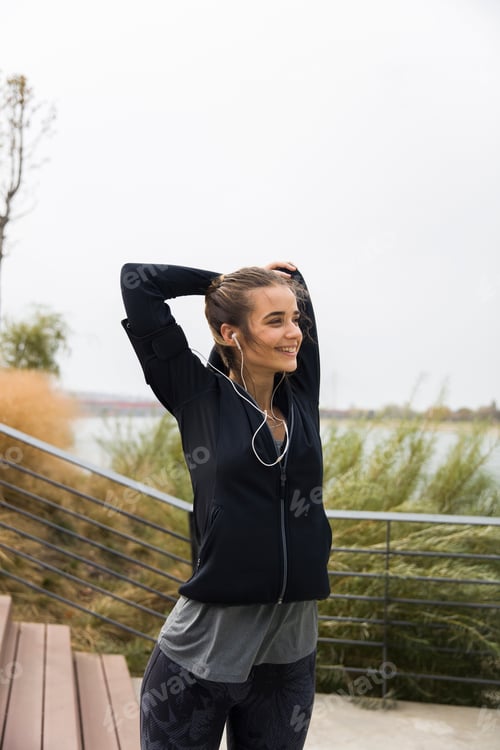 Preview: Female athlete stretching her arms while listening to music outdoors
