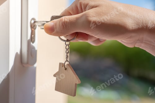 Preview: Opening door to a new home with key and home shaped keychain. Property and new home concept