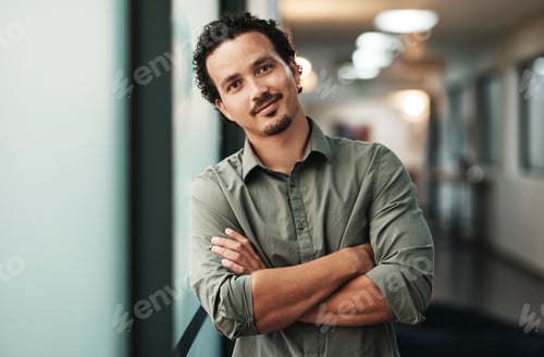 Preview: Shot of a handsome young businessman standing alone in the office with his arms folded