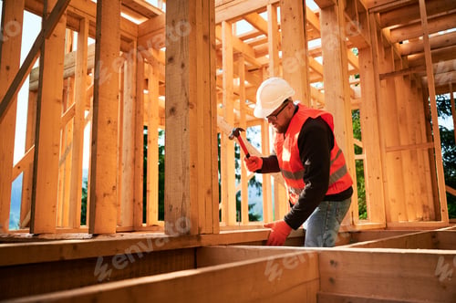 Preview: Carpenter hammering nail while constructing wooden frame two-story house near the forest.