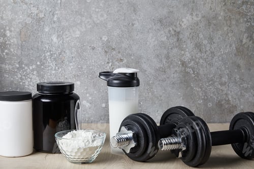 Preview: dumbbells near protein shake in sports bottle and protein powder near concrete wall