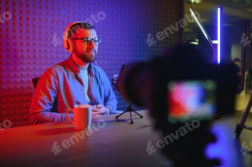Preview: Young man recording or streaming podcast using microphone at his small broadcast studio.