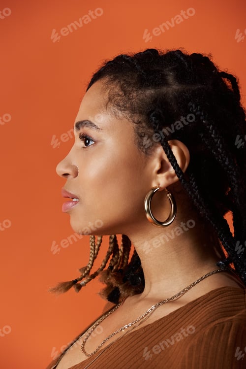 Preview: Young African American woman with braids posing in a studio with an orange backdrop