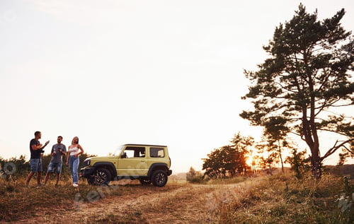 Preview: Rural scene. Group of cheerful friends have nice weekend at sunny day near theirs green car outdoors