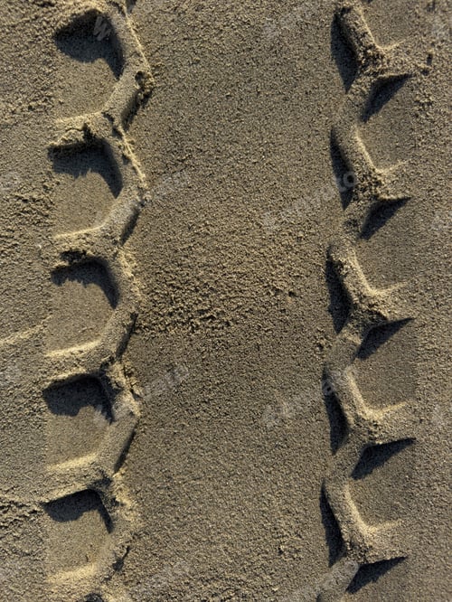 Preview: Close-up detail of a geometric pattern of tire tracks on sand