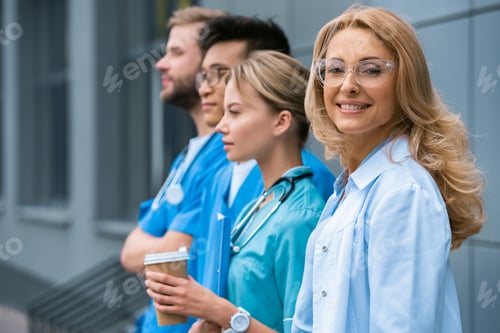 Preview: smiling teacher with multicultural students standing in row near medical university