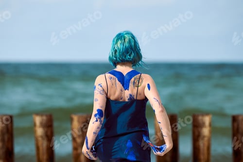Preview: Artistic blue-haired woman performance artist in dress smeared with blue gouache paints on her body